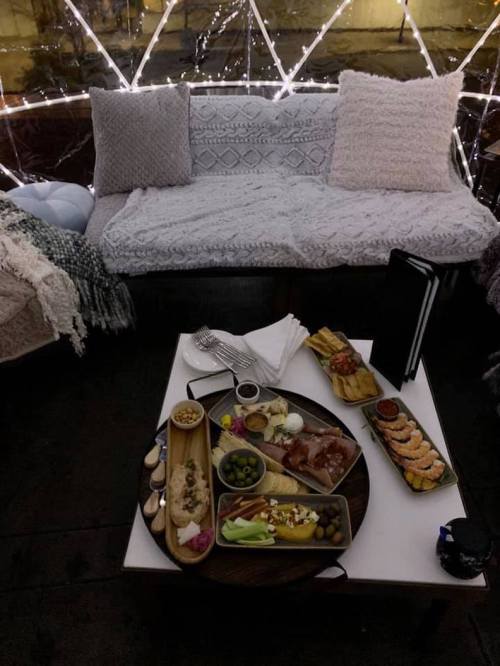 Cozy dining setup with a variety of dishes on a table, surrounded by soft blankets and fairy lights.