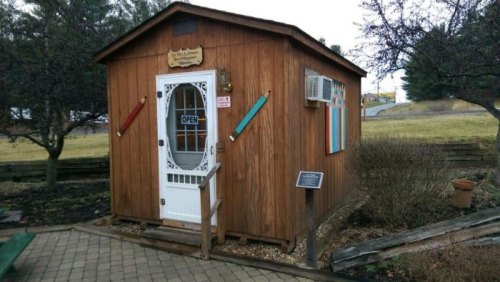 A small wooden shed with a sign that says "Open," surrounded by grass and trees.