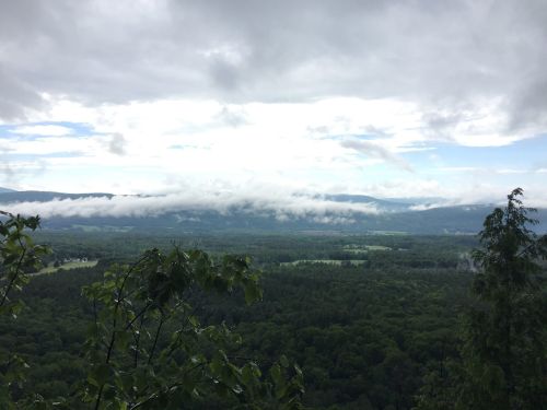 A panoramic view of a lush green valley under a cloudy sky, with mist rolling over distant mountains.