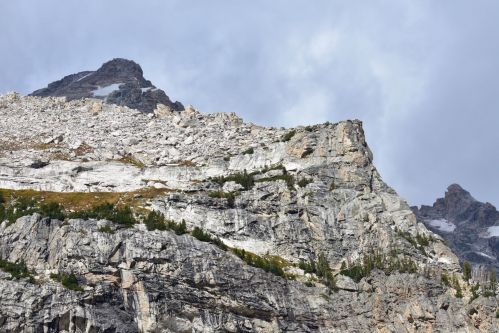 A rugged mountain landscape with rocky cliffs and patches of greenery under a cloudy sky.