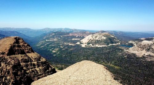 A panoramic view of rugged mountains and valleys under a clear blue sky, showcasing lush greenery and distant peaks.