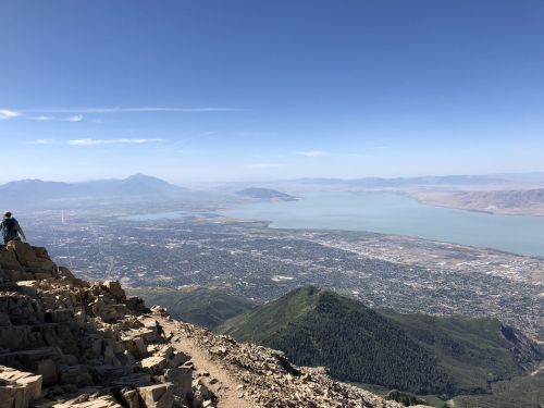 A panoramic view from a mountain peak overlooking a lake and a city below, with clear blue skies.