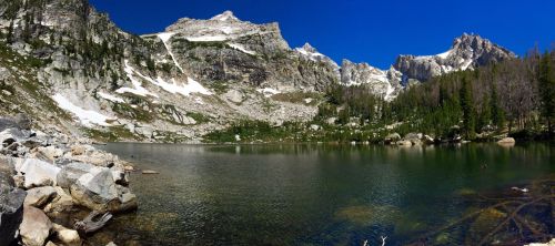 A serene mountain lake surrounded by rocky terrain and snow-capped peaks under a clear blue sky.
