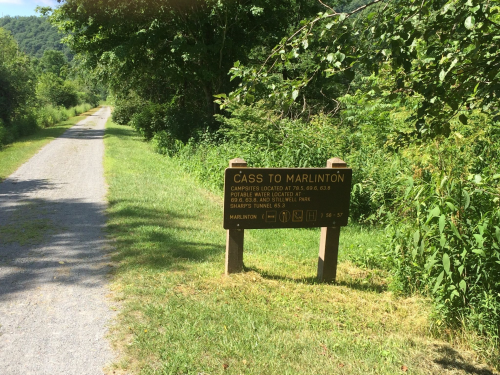 Sign for the Cass to Marlinton trail, with information on campsites and amenities, surrounded by greenery.