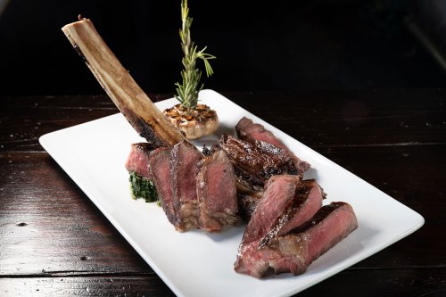 A beautifully plated dish featuring a large bone-in steak, sliced and garnished with herbs on a white plate.