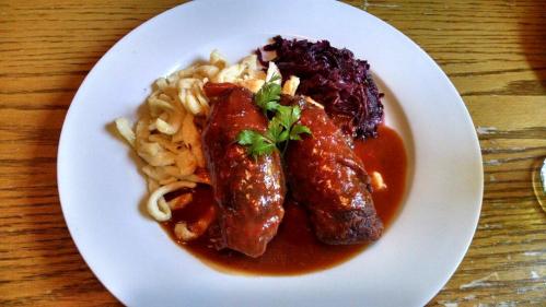 A plate featuring two stuffed cabbage rolls in sauce, served with noodles and red cabbage.