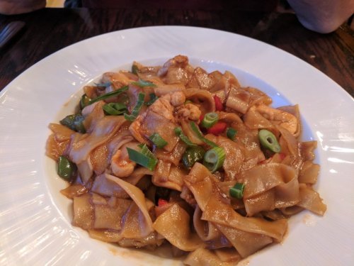 A plate of stir-fried flat noodles with chicken, bell peppers, and green onions on a white dish.
