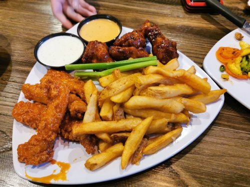 A platter of crispy chicken wings with two dipping sauces, celery sticks, and a side of golden French fries.