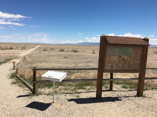 A signpost and mailbox in a vast, dry landscape under a clear blue sky, with a distant path leading into the horizon.