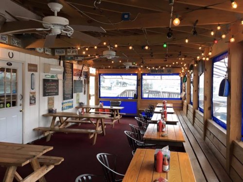 Cozy restaurant interior with wooden tables, string lights, and a view of the outdoors through large windows.