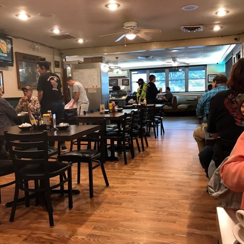 A cozy diner interior with wooden floors, tables, and patrons enjoying meals. Staff are serving food in the background.