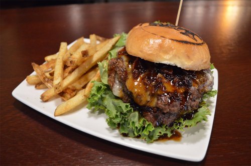 A juicy burger with melted cheese and sauce on a bed of lettuce, served with crispy fries on the side.