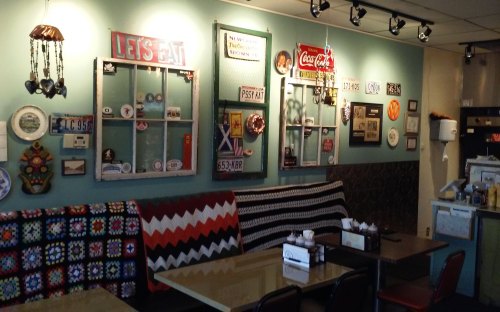 A cozy café interior featuring colorful wall decor, vintage signs, and patterned blankets on the seating.