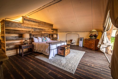Cozy tent interior featuring a wooden accent wall, a bed, dresser, and rustic decor on a wooden floor.