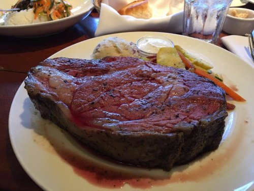 A juicy prime rib steak served with mashed potatoes and mixed vegetables on a white plate.