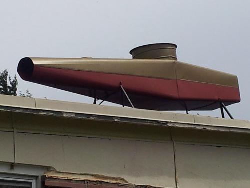 A large, decorative vent resembling a vintage aircraft, painted gold and red, sits atop a building.