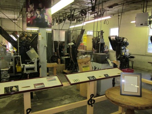A workshop with machinery and displays, featuring people working and informational panels in a well-lit space.