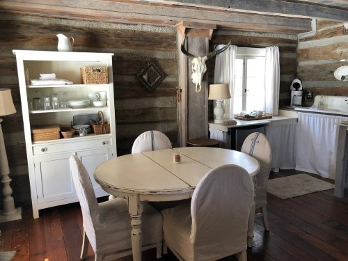 Cozy rustic kitchen with a round table, white chairs, wooden beams, and a vintage decor featuring a deer skull.