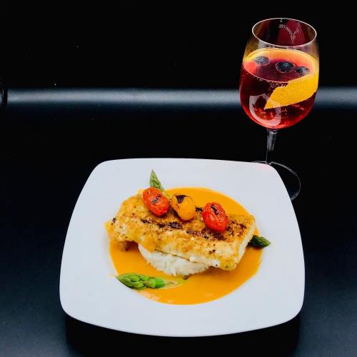 A plate of grilled fish with cherry tomatoes on a bed of rice, accompanied by a colorful drink with fruit garnish.