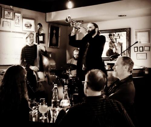 A jazz band performs in a cozy venue while an audience enjoys the music at a table.
