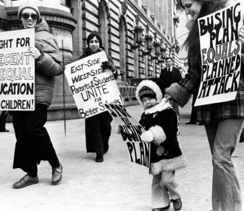 Black and white photo of protesters, including a child, holding signs advocating for equal education and better schools.