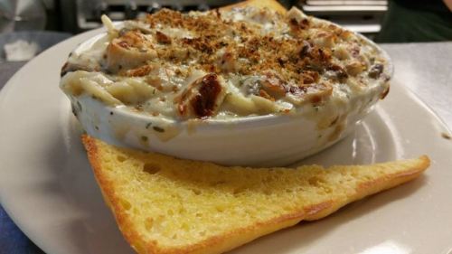A creamy seafood casserole topped with breadcrumbs, served with a slice of golden cornbread on the side.