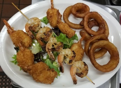 A plate of fried shrimp, grilled shrimp on skewers, and onion rings served on a bed of lettuce.