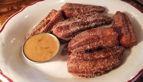A plate of cinnamon-sugar coated churros served with a small cup of dipping sauce.