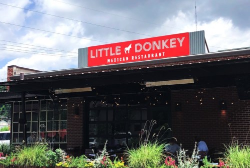 Exterior of Little Donkey Mexican Restaurant with a bright red sign and outdoor seating surrounded by plants.