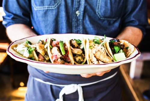 A person holding a platter of assorted tacos topped with fresh ingredients and garnishes.
