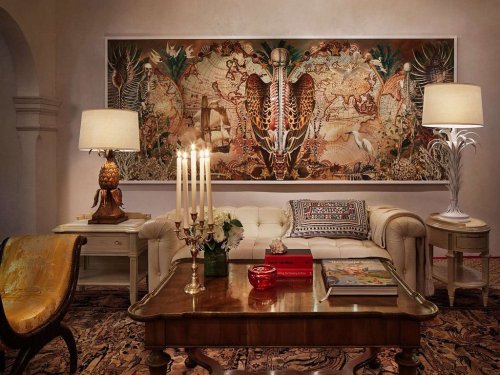 A stylish living room featuring a large tapestry, elegant furniture, and decorative lamps, creating a cozy atmosphere.