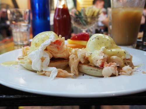 A plate of eggs Benedict topped with crab meat, served with a side of fruit and drinks in a lively restaurant setting.