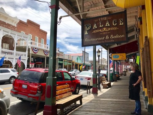 A street view of a historic town featuring a restaurant sign, parked cars, and a person standing on the sidewalk.