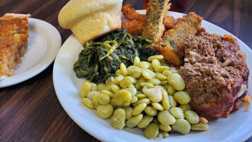 A plate of comfort food featuring meatloaf, collard greens, lima beans, fried okra, a biscuit, and a slice of pie.