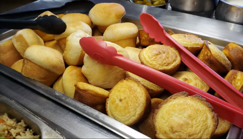 A tray filled with golden-brown muffins and cornbread, with red tongs resting on top.