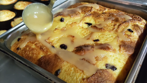 A freshly baked dessert drizzled with a creamy sauce, featuring a golden-brown top and dark raisins.
