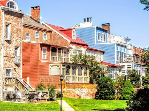 Colorful row of historic houses with porches and manicured lawns under a clear blue sky.