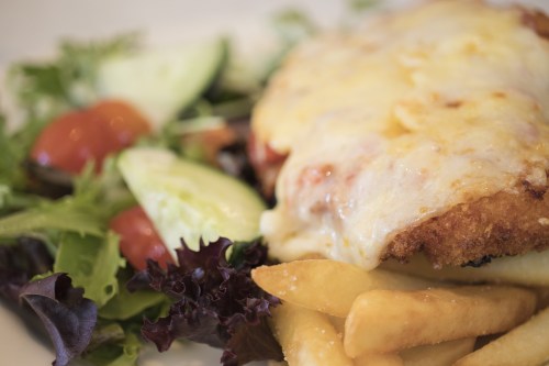 A plate featuring a cheesy chicken dish, crispy fries, and a fresh salad with tomatoes and cucumbers.