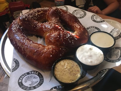 A large, soft pretzel on a tray with three dipping sauces: mustard, cheese, and ranch.
