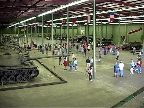 A large indoor museum displaying tanks, with many visitors exploring the exhibits and flags hanging from the ceiling.