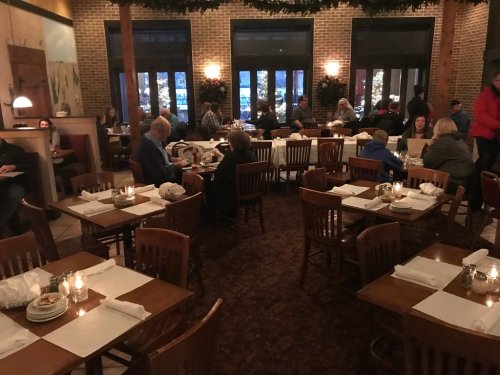 Cozy restaurant interior with wooden tables, chairs, and diners enjoying their meals in a warm, festive atmosphere.