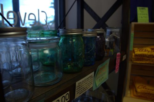 A shelf displaying various glass jars in different colors and sizes, with price tags visible.
