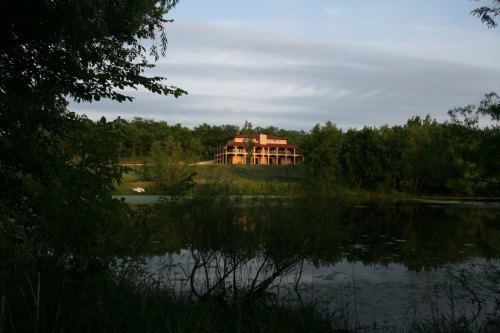 A serene landscape featuring a house on a hill, surrounded by trees and reflecting in a calm pond.