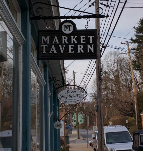 Signage for Market Tavern and Sweet Simpli-Tea, with a view of a street lined with power lines and trees.