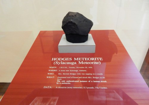 A dark meteorite displayed on a pedestal with an informational plaque about the Hodges Meteorite.