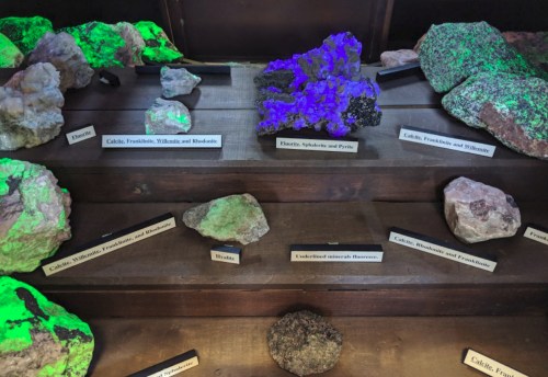A display of various minerals and rocks, some glowing under UV light, with labels identifying each specimen.