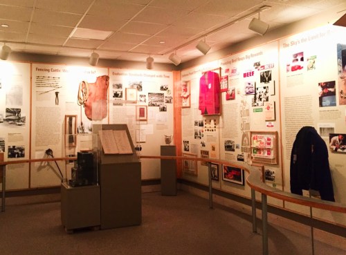 Exhibit room featuring historical displays, photos, and artifacts on walls, with a central display case.