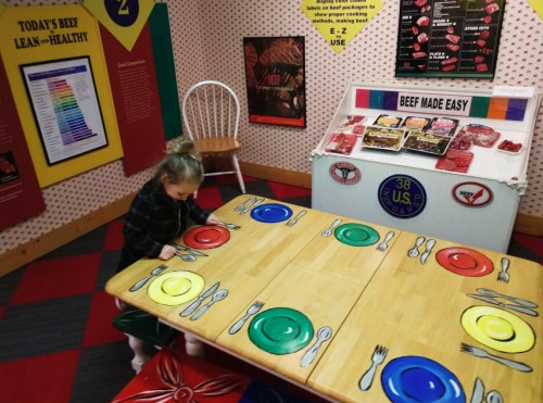 A child sets a colorful table in a playful educational space about beef and healthy eating.