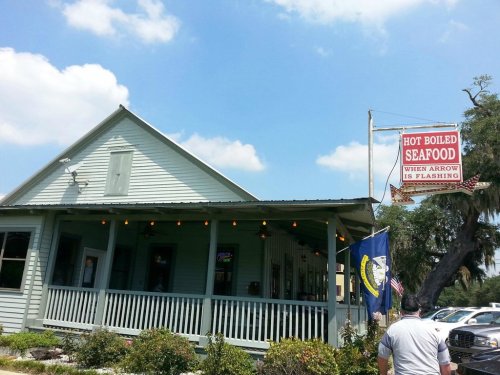 A seafood restaurant with a sign reading "Hot Boiled Seafood" and a flashing arrow, set against a blue sky.