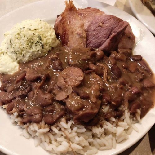 A plate of rice topped with beans, ham, and a side of creamy mashed potatoes.